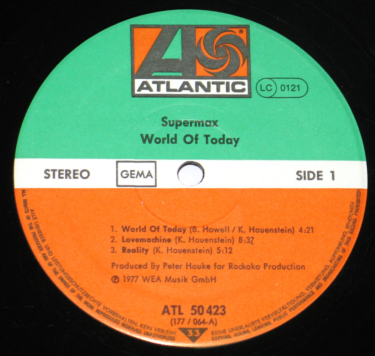 Close-up of the record label for SUPERMAX - World of Today (1977), Side One. The label features the iconic green, white, and orange Atlantic Records design, with the bold 'A' logo at the top. It includes track listings, production credits, and catalog information, with 'Stereo' and 'GEMA' markings. The center hole is visible, with black vinyl surrounding the label.