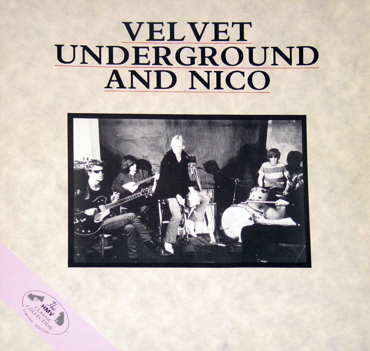 Front of the HMV Classic Collection limited edition cover for The Velvet Underground and Nico, showing a black-and-white band photo with Nico centered, surrounded by Lou Reed, Sterling Morrison, Maureen Tucker, and John Cale. The textured off-white background is overlaid with bold black and red-outlined text, and a lavender diagonal ribbon in the bottom-left corner states 'The HMV Classic Collection Limited Edition'.