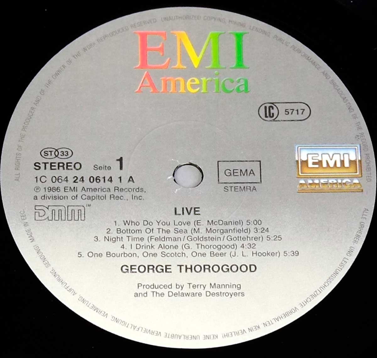 Side One label of George Thorogood & The Destroyers – Live LP, grey EMI America label with tracklist, DMM and GEMA markings, catalog number 1C 064 24 0614 1A, and EMI logo in silver and gold.