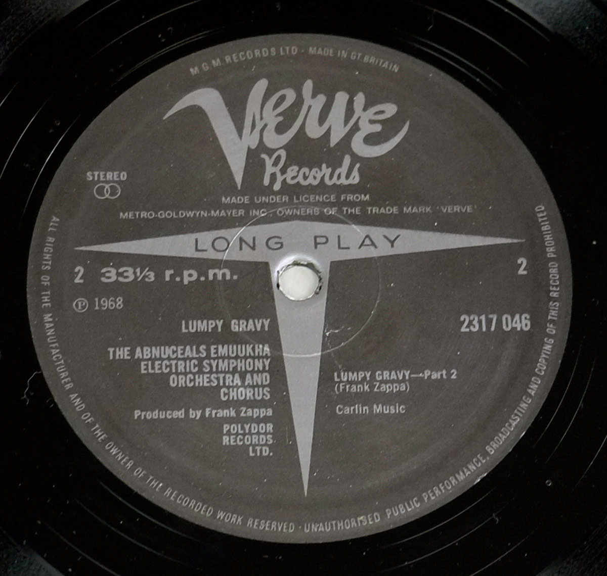 Close-up of the UK Verve Records Side Two label for “Lumpy Gravy,” showing a dark grey matte background with bright white text, the large Verve script logo, the LONG PLAY arrow graphic passing through the spindle hole, catalog number 2317 046, 33⅓ r.p.m. speed, and complete MGM licensing and UK manufacturing text around the rim.