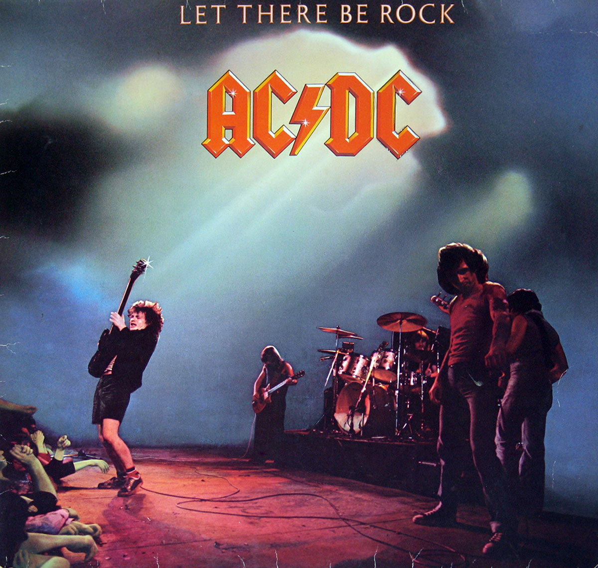 Dynamic live-action front cover of AC/DC’s “Let There Be Rock” German release, featuring Angus Young’s iconic guitar stance and Bon Scott’s commanding stage presence under dramatic lighting