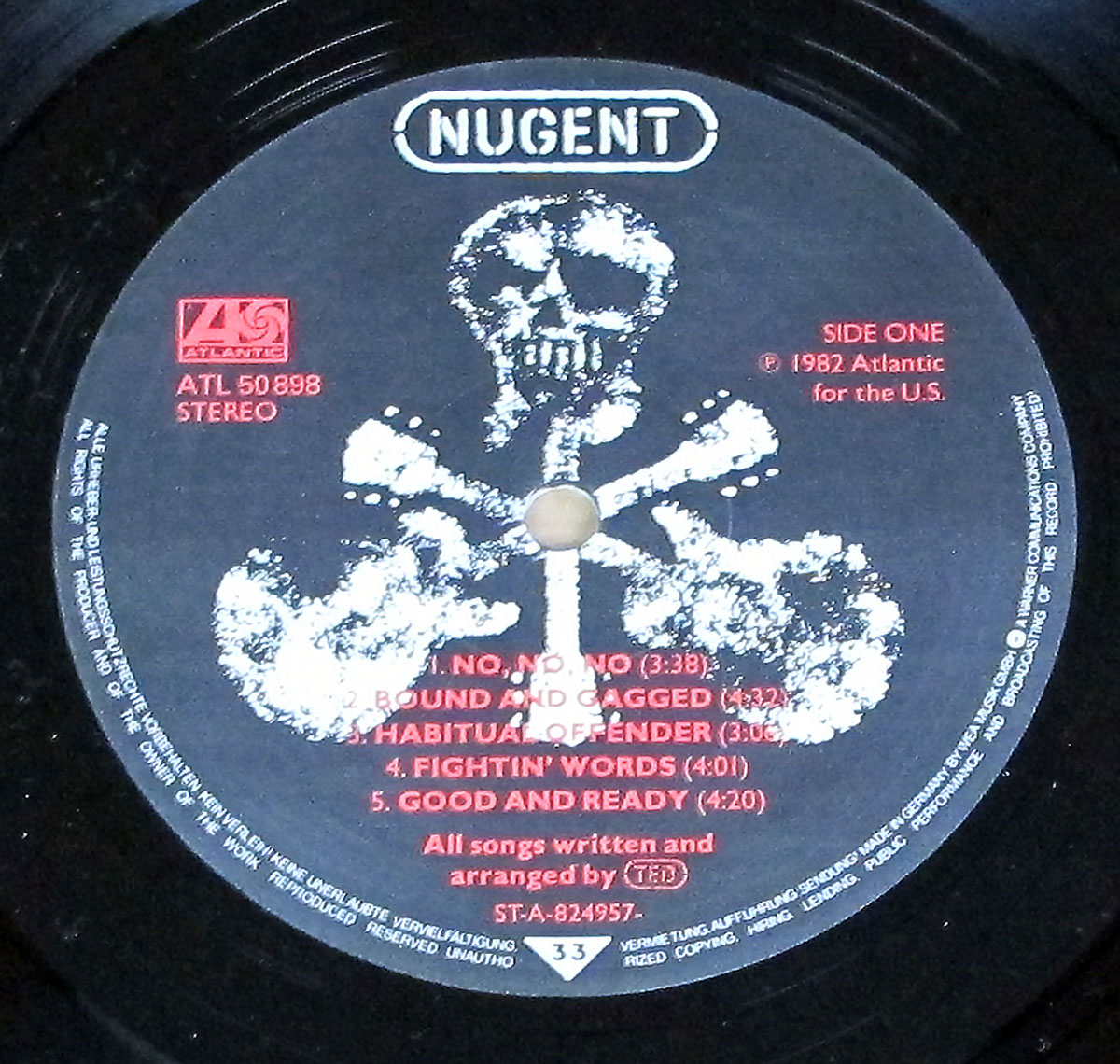 Close-up of Side One record label from the 1982 Ted Nugent album Nugent, Atlantic ATL 50 898, featuring a black background with a distressed white skull-and-crossbones graphic made from guitar silhouettes. The bold white 'Nugent' logo is centered at the top, with the Atlantic Records logo in red on the left. Track listings and credits appear in red and white text, including five song titles, copyright, catalog number, and arrangement credits.