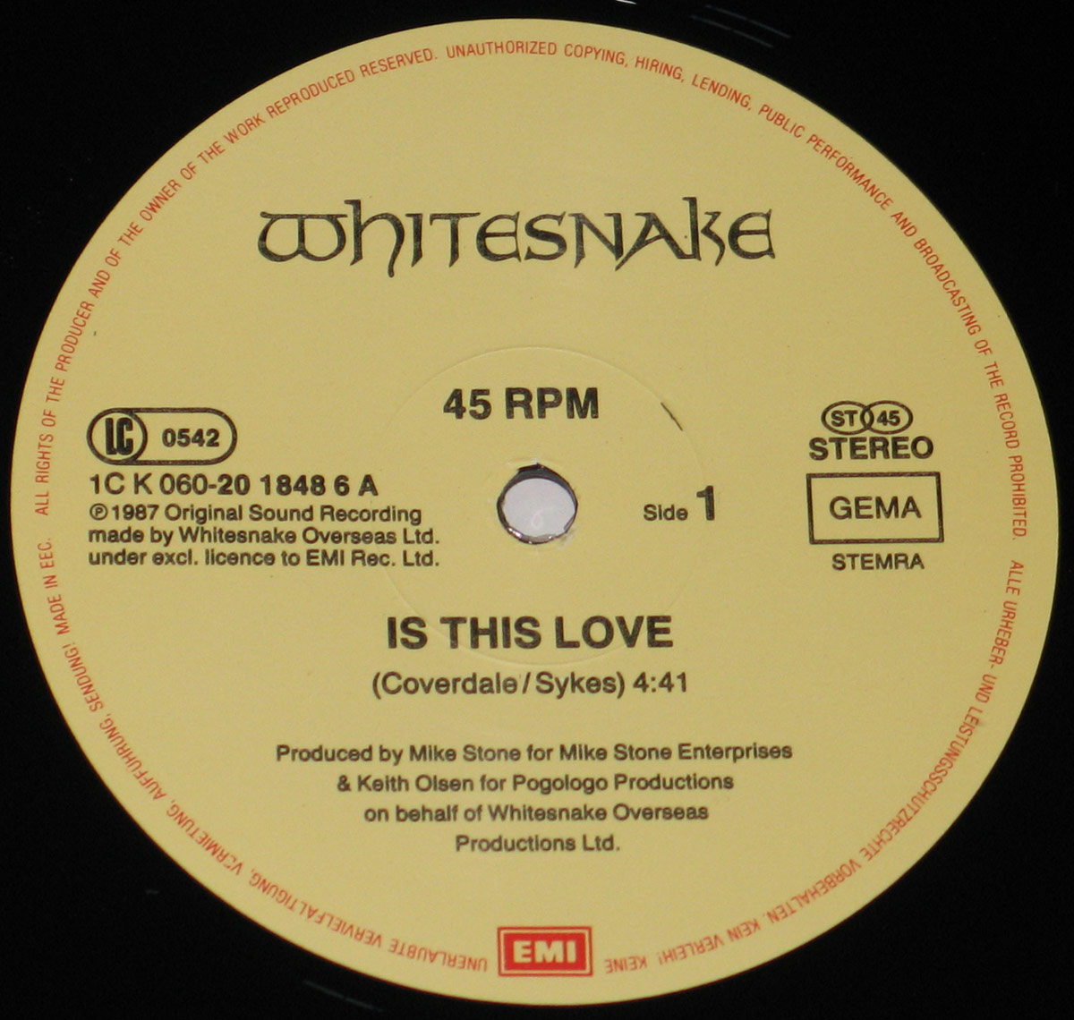 Close-up of the Side One record label of Whitesnake’s 12-inch Maxi-Single 'Is This Love', pressed by EMI in 1987. The label features a soft cream background with clean black typography. At the top, the iconic Whitesnake logo is printed in bold gothic lettering, while below it the title 'Is This Love' is credited to Coverdale and Sykes. Production details for Mike Stone and Keith Olsen are printed in the lower half, alongside EMI’s red rectangular logo at the bottom. The outer rim contains fine circular text stating copyright and manufacturing rights, characteristic of 1980s European pressings.