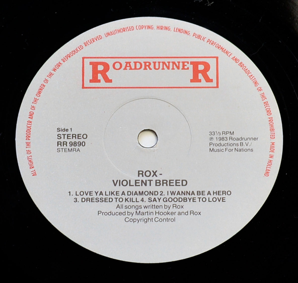 Close up of Record label of Rox’s Violent Breed album featuring a white background with the red Roadrunner Records logo at the top, black text displaying the album title and band name in the center, and production details. Red copyright text encircles the edge, indicating it was made in Holland.