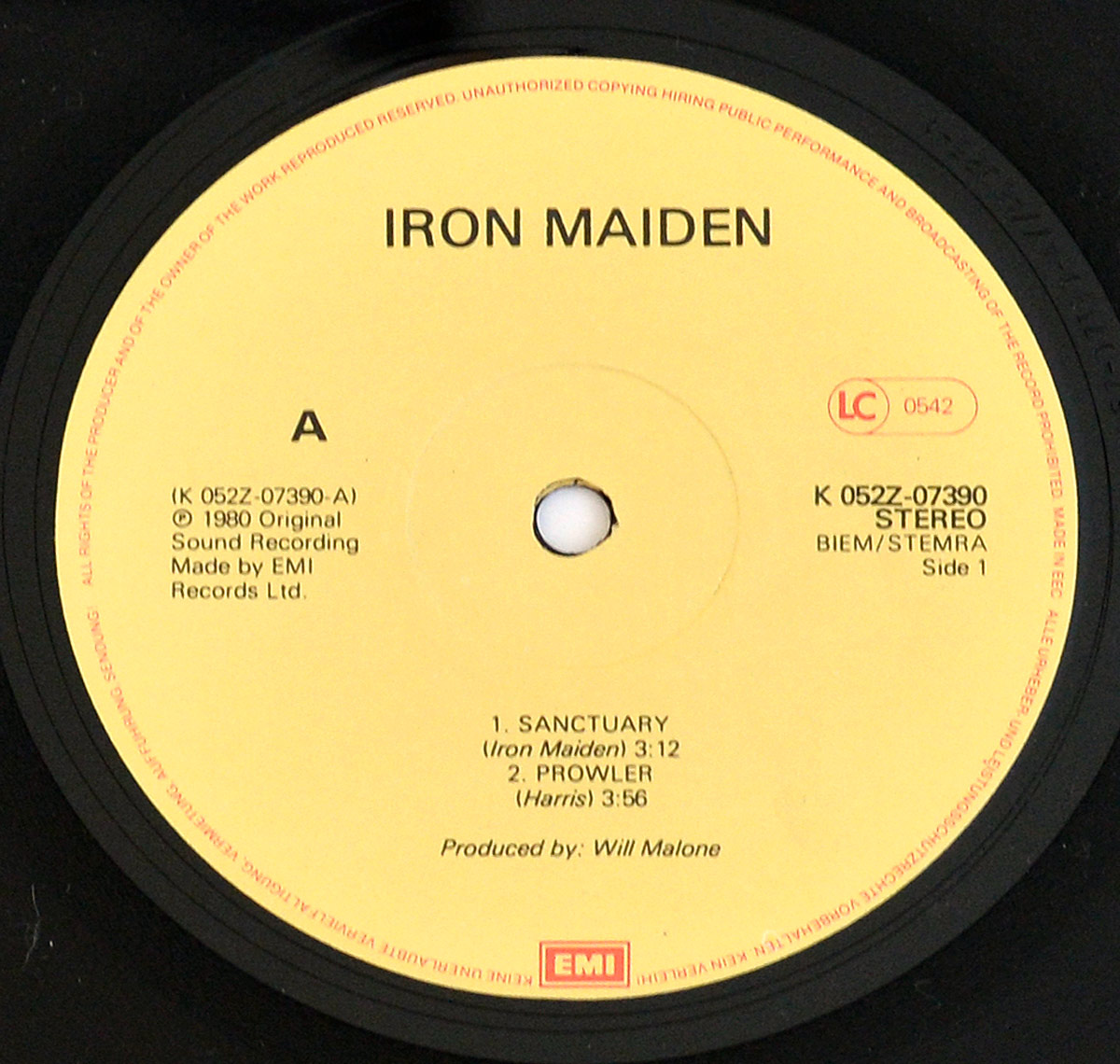 Close-up of Iron Maiden Sanctuary EP Netherlands Side One vinyl label, pale yellow EMI label with black text, red LC 0542 marking on right, spindle hole centered with slight wear, track listing Sanctuary and Prowler below, BIEM STEMRA rights text and K 052Z-07390 catalogue number visible, black vinyl grooves surrounding label