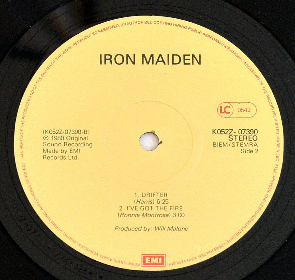 Close-up of Iron Maiden Sanctuary EP Netherlands Side Two vinyl label, pale yellow EMI label with black text, red LC 0542 marking on right, spindle hole centered with visible wear, track listing Drifter and I've Got The Fire below, BIEM STEMRA text and catalogue number K 052Z-07390 present, surrounded by black vinyl grooves with light reflections