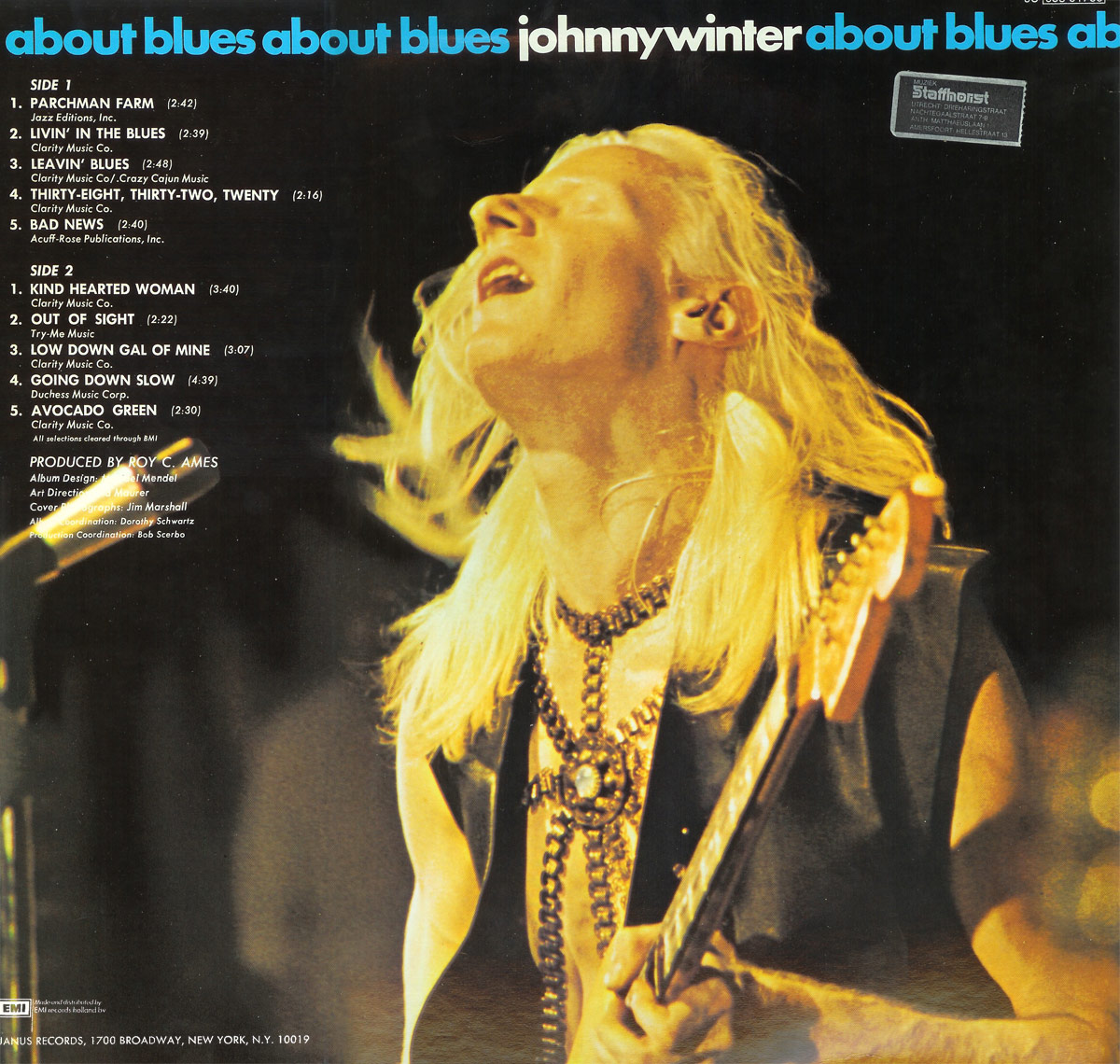 Back cover of About Blues by Johnny Winter. A warm, golden-toned photograph of Johnny Winter mid-performance, head tilted back, eyes closed, and long blonde hair flowing. He wears a black leather vest and layered silver necklaces while gripping his Fender guitar. The album title ‘about blues’ repeats in blue and white text along the top. The left side features the tracklist in white text, along with production credits. A small Staffhorst sticker appears in the upper right corner, and the EMI and Janus Records logos are visible at the bottom left