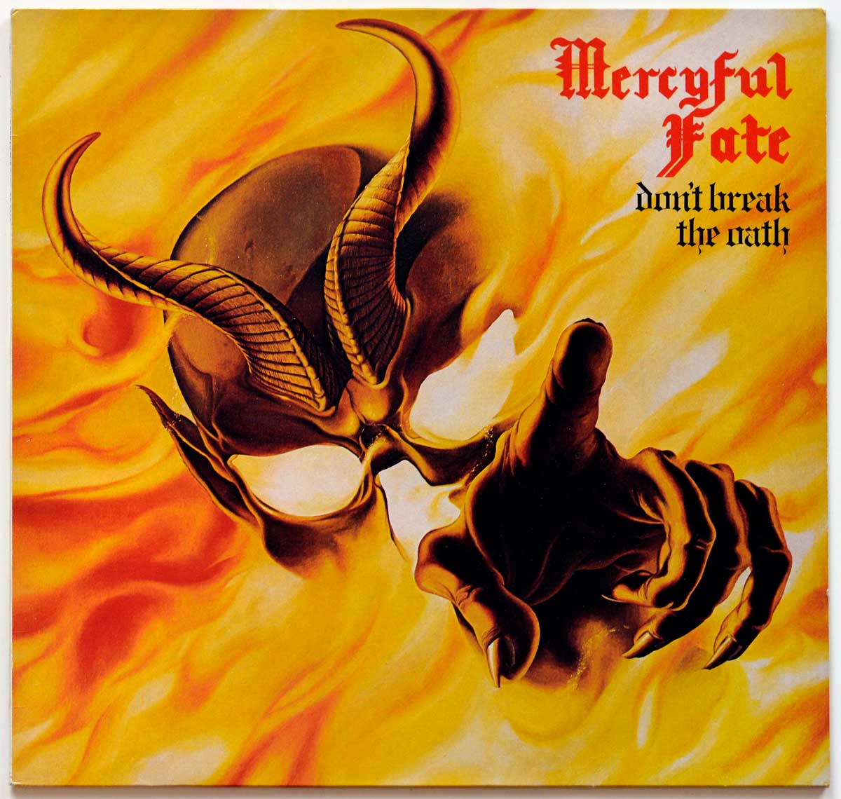 The album cover for &quote;Don't Break the Oath&quote; by Mercyful Fate features a dark, fiery design. A skeletal, demonic figure with hollow, glowing eyes and large, twisted horns stares directly ahead. The figure extends a long, clawed finger toward the viewer, creating an intense, unsettling effect. The background is engulfed in swirling flames, with vivid shades of yellow, orange, and red that enhance the infernal atmosphere. In the top right corner, the band’s name, *Mercyful Fate*, appears in a blood-red, gothic-style font, and the album title, &quote;Don't Break the Oath&quote;, is below it in a blackletter font. The artwork captures themes of horror and mysticism, reflecting the dark, heavy music within. https://vinyl-records.nl 