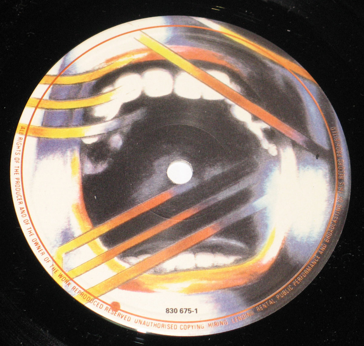 Close-up of the Side One record label for Def Leppard’s 1987 album Hysteria on Mercury/Bludgeon Riffola. The design features a screaming open mouth rendered in surreal, painterly tones of white, blue, orange, and yellow, intersected by diagonal orange beams. The catalog number 830 675-1 appears at the bottom rim, and fine orange text circles the edge detailing copyright and production rights.