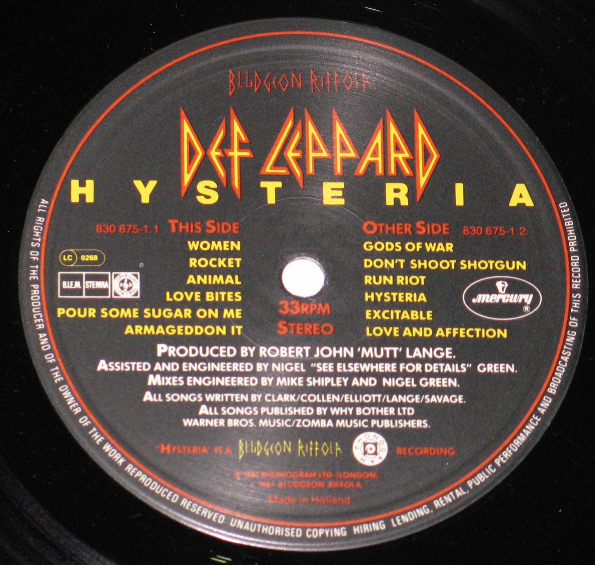 Close-up of the Side Two record label for Def Leppard’s 1987 album Hysteria on Bludgeon Riffola and Mercury. The black label features the red-and-yellow Def Leppard logo at the top, track listings for both sides in orange and yellow text, and full production credits including producer Robert John 'Mutt' Lange. The Mercury logo appears on the right, with catalog numbers 830 675-1.1 and 830 675-1.2 and Made in Holland at the bottom.