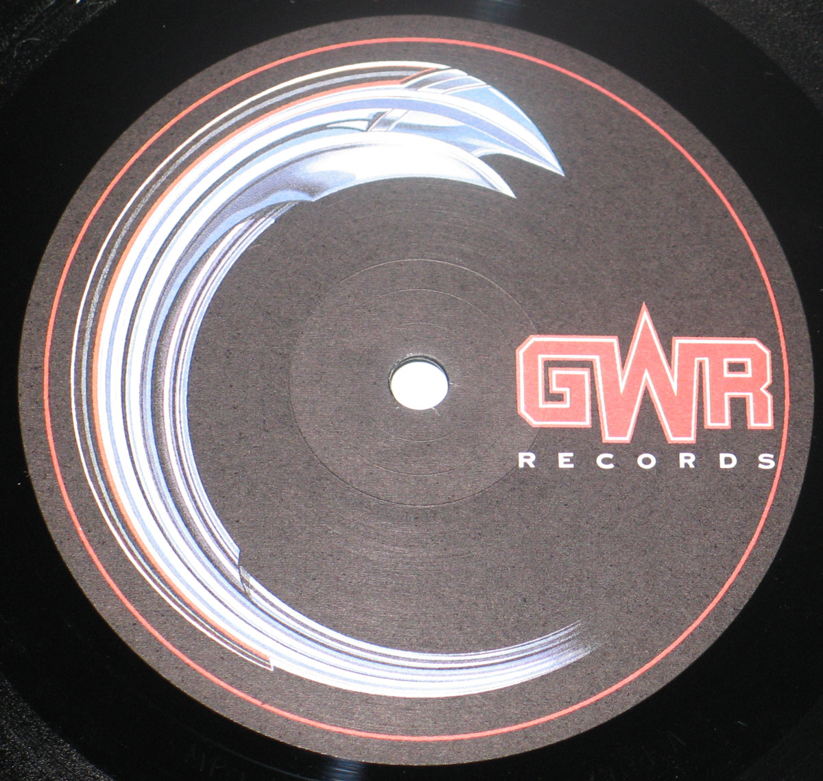 Close-up of the Side One record label from Motörhead "Orgasmatron", showing a dark GWR Records label on black vinyl. A large metallic silver and blue curved blade-like graphic sweeps around the left side, with a thin red circular border near the edge. The red GWR Records logo sits on the right, beside the centre spindle hole.
