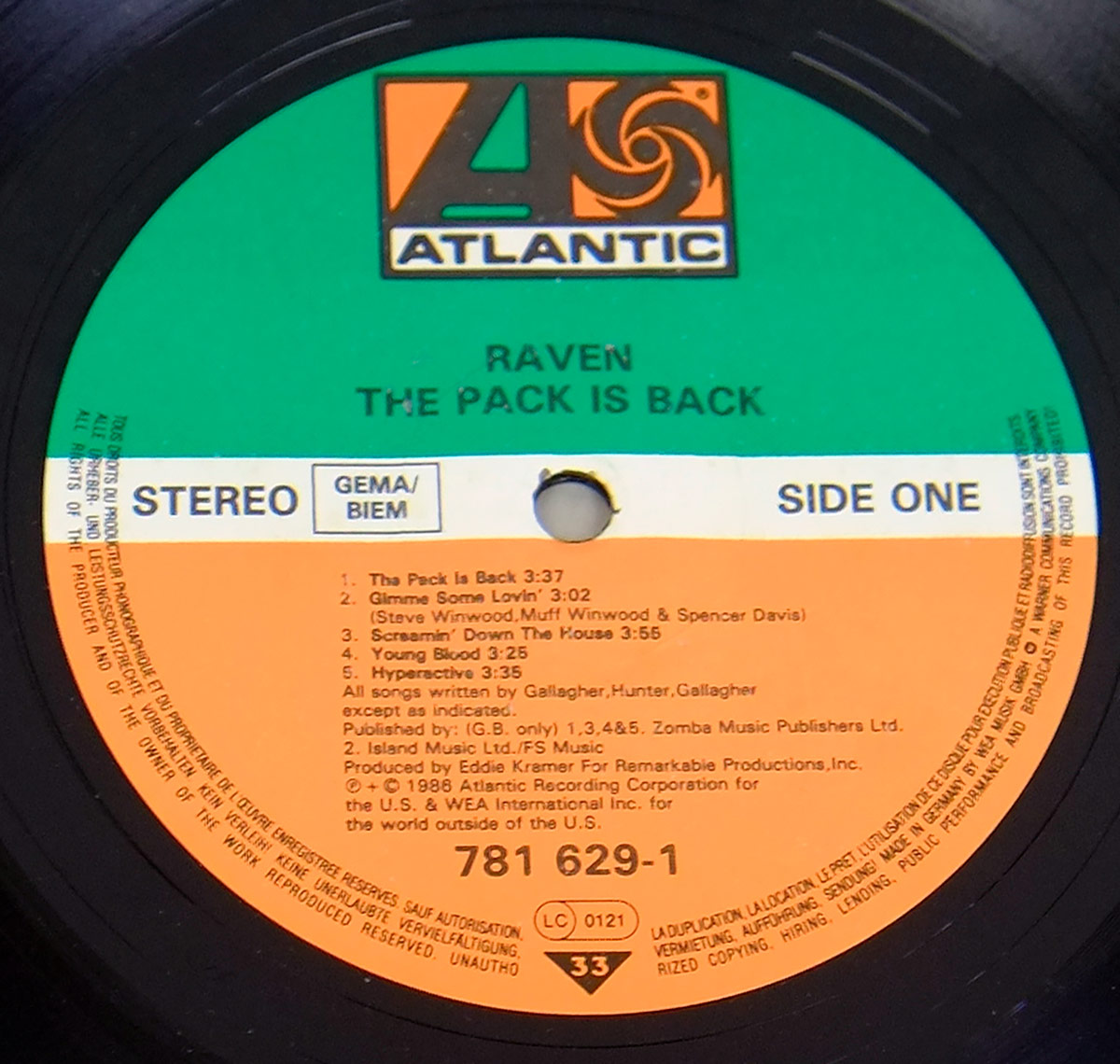 Close-up of Side One label for Raven The Pack Is Back on Atlantic Records. The label has a green upper half, white centre band and orange lower half, with the Atlantic logo at the top. It shows RAVEN, THE PACK IS BACK, STEREO, GEMA/BIEM, SIDE ONE, five track titles with timings, catalogue number 781 629-1, LC 0121, 33 speed mark and multilingual rim text.