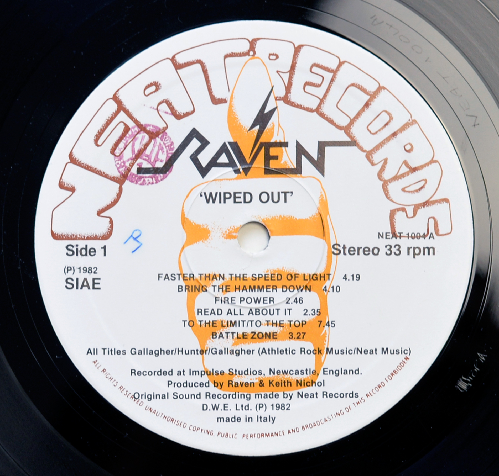 Close-up of Raven Wiped Out Side 1 record label on black vinyl, showing a white Neat Records label with the large brown Neat Records logo curved across the top, the Raven logo and orange lightning-bolt drawing in the centre, Side 1 on the left, NEAT 1004 A and Stereo 33 rpm on the right, SIAE rights mark, track titles, production credits, made in Italy text, and stamped matrix detail in the run-out groove.