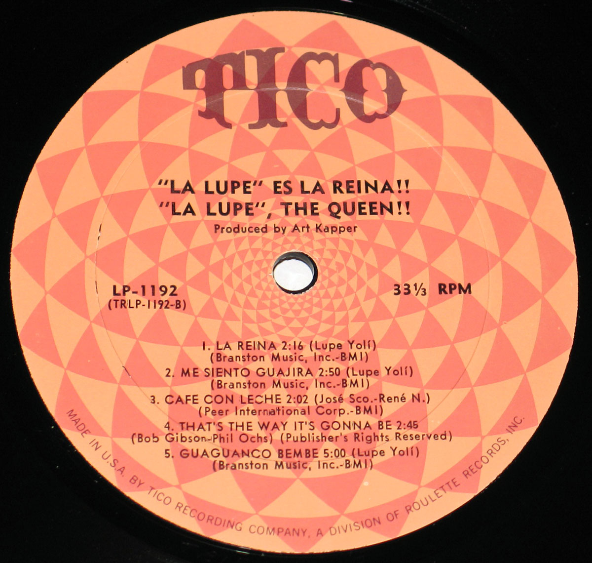 Close-up of the Side B record label for La Lupe – Es La Reine (The Queen), Tico Records LP-1192 (TRLP-1192-B). The circular label features a vivid orange and red hypnotic spiral pattern with the bold TICO logo printed at the top in brown. Text at the center identifies the album title 'La Lupe Es La Reina!! La Lupe The Queen!!' produced by Art Kapper, with catalog details LP-1192 and 33⅓ RPM speed. The song list for Side B is printed below in black lettering, including 'La Reina,' 'Me Siento Guajira,' 'Café Con Leche,' 'That’s The Way It’s Gonna Be,' and 'Guaguancó Bembé,' along with composer credits such as Lupe Yoli, José Sco., René N., Bob Gibson, Phil Ochs, and publishing companies Branston Music and Peer International Corp. Around the edge, small text reads 'Made in U.S.A. by Tico Recording Company, a Division of Roulette Records, Inc.'