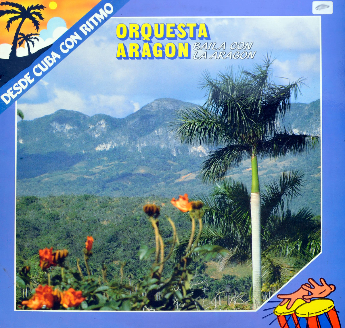 Front cover of the Orquesta Aragon album Baila Con La Aragon from the series Desde Cuba Con Ritmo, showing a vivid landscape with mountains, palm trees, orange flowers and a blue frame with tropical icons.