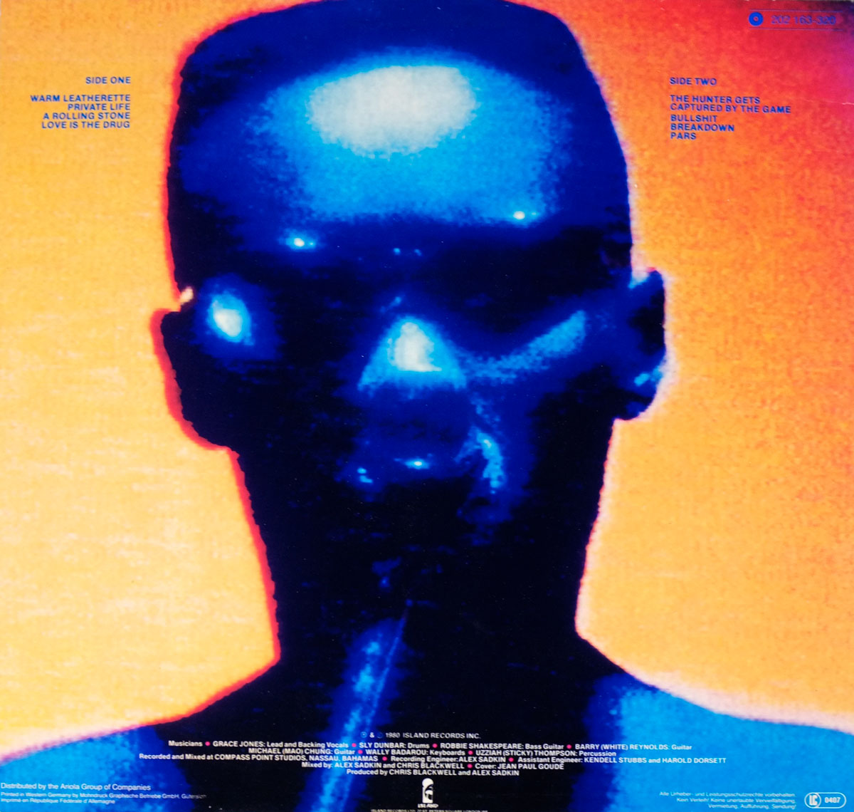 The back cover of Grace Jones’ 1980 album Warm Leatherette. The design features a surreal, high-contrast blue and black portrait of Jones’ face, photographed from the front and rendered with glowing effects. Her skin appears metallic blue with highlights on the forehead, nose, and cheeks, while her eyes and glasses reflect with intense light flares. The portrait floats against a vivid orange background, giving the impression of heat and energy. On the left, in small blue uppercase text, the Side One track list is printed: Warm Leatherette, Private Life, A Rolling Stone, Love Is the Drug. On the right, the Side Two track list is printed: The Hunter Gets Captured by the Game, Bullshit, Breakdown, Pars. Along the bottom edge, white text provides credits including musicians, producers Chris Blackwell and Alex Sadkin, and recording details at Compass Point Studios, Nassau, Bahamas. The Island Records logo appears centered at the bottom. The entire layout combines minimal typography with an intense, futuristic portrait style.