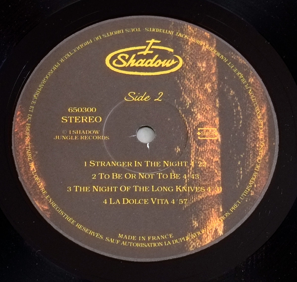 Close-up of Side Two vinyl label for I SHADOW – An I For An I, featuring golden serif text on a brown background with tracklist, catalog number 650300, and SUISA logo, decorated with a subtle paisley motif.