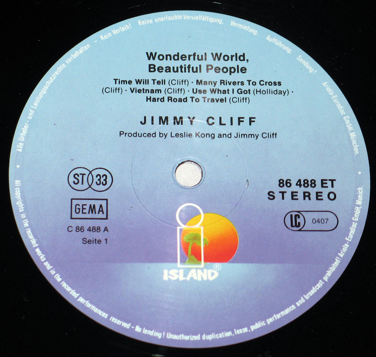 Close-up of the Side One record label for Jimmy Cliff's album Wonderful World, Beautiful People. The label is printed on a soft blue background with a gradient that darkens toward the edges. At the bottom center sits the Island Records logo, featuring a yellow sun setting behind a green palm tree within a white outlined square. Above the spindle hole, the album title is printed in bold black letters, followed by the track list for Side One: Time Will Tell, Many Rivers to Cross, Vietnam, Use What I Got, and Hard Road to Travel. Jimmy Cliff’s name is displayed prominently in uppercase letters, with production credits to Leslie Kong and Jimmy Cliff. To the right, the catalog number 86 488 ET and the word STEREO are printed in black. Surrounding the outer edge are white circular text warnings against unauthorized duplication and lending. Additional identifiers include the ST 33 logo, GEMA rights society box, side designation C 86 488 A, and a small code number 0407 inside a circle. The design is both practical and emblematic of Island Records' 1970s aesthetic.