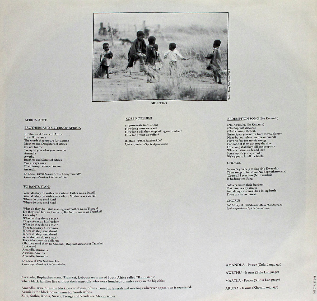 Back cover of Manfred Mann’s Earth Band 'Somewhere in Afrika', designed as a large, detailed political map of southern Africa during the apartheid era. The map spans the full cover, showing South Africa and its neighboring regions with borders sharply outlined in purple, highlighting territories labelled as Bantustans such as Transkei, Ciskei, Bophuthatswana, KwaZulu, Gazankulu, Lebowa, and QwaQwa. Major cities like Pretoria, Johannesburg, Durban, and Cape Town are marked, along with cross-border links to Botswana, Namibia, Zimbabwe, and Mozambique. Tracklisting text appears printed directly over the upper-left section of the map, divided into Side 1 and the Africa Suite, listing songs such as Tribal Statistics, Eyes of Nostradamus, Third World Service, Brothers and Sisters of Azania, and Redemption Song (No Kwazulu). Below the tracklist sits a block of production credits naming musicians and roles. Additional narrative text titled 'The City' appears at the bottom left like a vignette or short story. A small inset map in the lower right shows the Witwatersrand region. Catalogue numbers, distribution notes, and a yellow “Code 65” price label appear in the top-right corner, giving the cover a documentary, socio-political atmosphere.