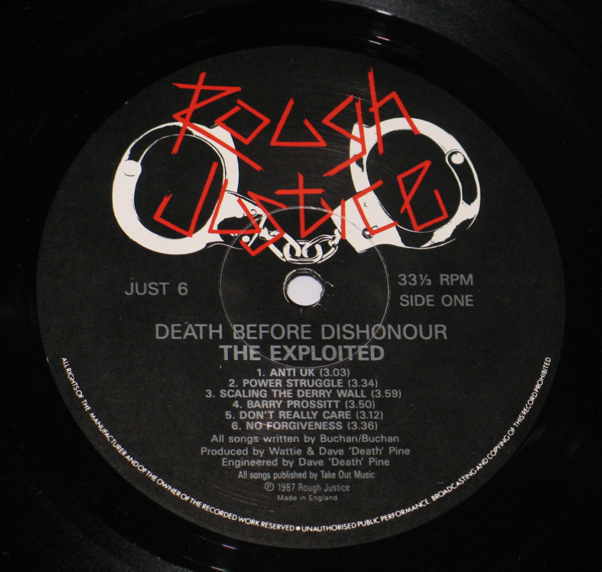 Vinyl record label for The Exploited's 'Death Before Dishonour' album, featuring the Rough Justice logo in red graffiti-style text over a black background with white handcuff graphics. The tracklist for Side One is displayed in white, along with production credits and copyright details.