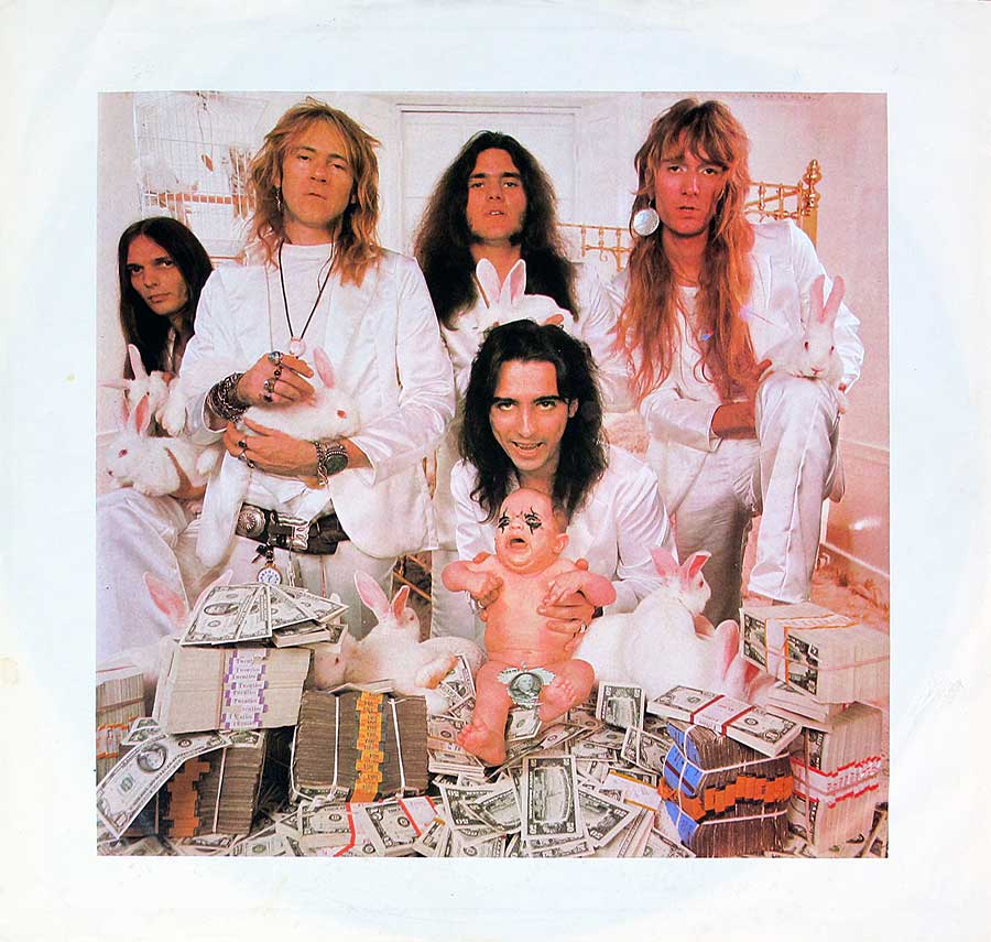 Group photo of th Alice Cooper band with Alice Cooper holding a baby and the band-members white rabbits 