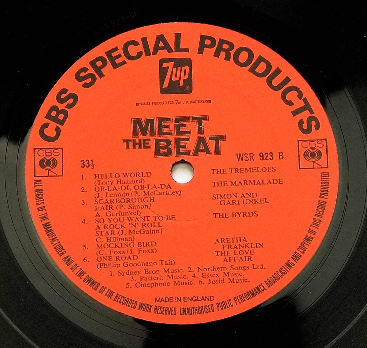 Close-up of Side Two label for the compilation album Various Artists Meet The Beat 7Up. The label is bright red with black print, framed around the edge by the words CBS SPECIAL PRODUCTS. At the top center sits the green-and-white 7UP logo inside a black rectangle, with the words 'Especially produced for 7up Ltd. (Switzerland)' below. In bold block type, the title MEET THE BEAT is centered above the spindle hole. On the right side, the catalog number WSR 923 B is shown alongside a CBS square logo. The tracklist is printed in two columns: on the left are song titles and songwriting credits, on the right are the performing artists. Side Two includes: Hello World (The Tremeloes), Ob-La-Di, Ob-La-Da (The Marmalade), Scarborough Fair (Simon and Garfunkel), So You Want to Be a Rock 'n Roll Star (The Byrds), Mocking Bird (Aretha Franklin), and One Road (The Love Affair). At the bottom are publishing credits, Made in England, and copyright text encircling the outer rim.